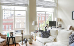 Bright living room with arched windows, white sofa, armchair, coffee table decor, lamps, photos. City view. Cozy modern vibe.