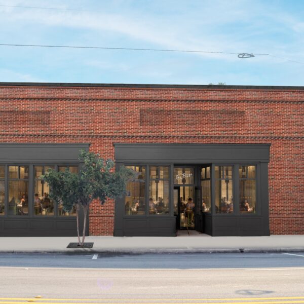 Brick building with large dark-framed windows, central entrance, arched side passage, tree and person on the sidewalk.