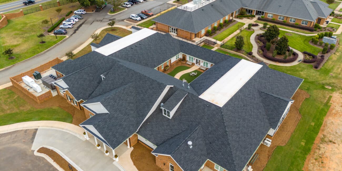 Aerial view of a modern brick building complex with dark gray roofs, green lawns, pathways, parking lots, and surrounding roads.